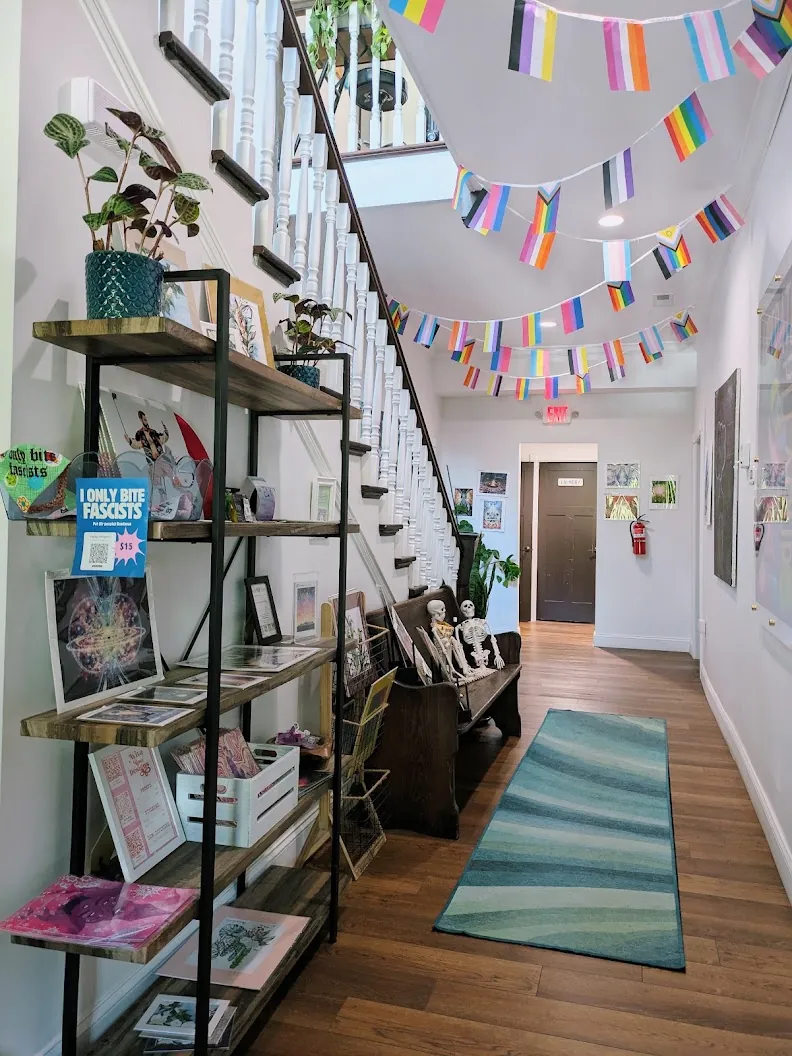 Inside Auroraflow, a colorful entryway with pride flag bunting, a reading bench, and a bookshelf